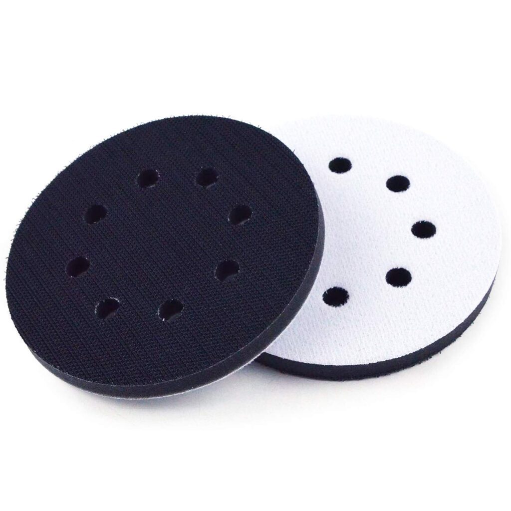 Two round sanding discs shown, one with a black surface with six holes and the other with a white surface having seven holes. Both have a hook-and-loop (velcro) type backing for attachment to a power sander.