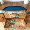 A Mid Century Beautility Drinks Cabinet, Vintage 1960's Walnut Cocktail Bar with a drawer partially open, revealing a vibrant peacock design on the inside. The exterior boasts a mid-century design with a natural wood finish and a blue accent on the top shelf. Pink flowers in a vase are elegantly placed on top of the cabinet.