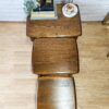 A top-down view showcases a set of three nesting G-Plan Astro Round Coffee Tables, Mid-Century Vintage. The smallest table displays a plant, a stack of books, and a decorative item. These tables rest on a hardwood floor with a white brick wall serving as the backdrop.