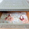 A wooden drawer from the Faux Bone Inlay Stencil Hand-Painted Vintage Chest of Drawers is partially open, showcasing an intricate floral and bird pattern inside. The exterior of the drawer features a decorative green and white design with geometric and floral elements. The drawer is placed on a wooden floor against a white brick wall background.