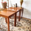 The Ercol Saville Ash Long Coffee Table with Smoked Glass Mid Century Vintage is placed on an ornate rug with brown and beige patterns. On the table, there is a tall, golden vase, a ceramic dog figurine, and a candle. In the background, there's a chair with a basket of pink flowers.