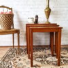 An Ercol Saville Ash Long Coffee Table with Smoked Glass Mid Century Vintage is arranged on a decorative rug with intricate patterns against a white brick wall. On the table, there are a tall brass vase, a small candle, and a ceramic figurine. A woven basket on a chair is partially visible on the left.