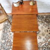 An Ercol Saville Ash Long Coffee Table with Smoked Glass Mid Century Vintage is positioned on a decorative rug. On its surface, there is a bronze dog figurine, a brass vase, and a candle. To the side, part of a wooden chair with a woven seat is visible.