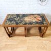 A G Plan Astro Long John Teak Nest of Tables featuring rectangular wooden tables with curved legs and an artistic top surface design. The detailed design showcases a leopard amid a pattern of gold-colored leaves on a dark background, all set against a light wooden floor.