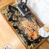 A G Plan Astro Long John teak coffee table featuring a detailed leopard image on its surface, surrounded by gold accents. On the table are books, a small figurine, a potted plant, and a marble-topped item. The floor is wooden, and the wall behind is white brick.