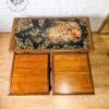 Vintage wooden side table from the G Plan Astro Long John Teak Nest Of Tables collection, featuring intricate artwork of a leopard on its black tabletop. Below the tabletop is a single drawer front. The scene includes wooden floors and a light-colored brick wall in the background, with part of a golden framed mirror visible on the right side.