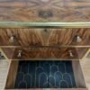 A wooden dresser with a decorative grain pattern, gold trim, and round gold knobs. The bottom drawer is open, revealing a black lining with gold geometric patterns. There is a logo on the top surface that says "Flip & Restore!" with a small circular saw and paintbrush.