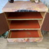 A hand-painted cabinet, standing tall as a versatile linen cupboard, has its doors open to reveal three striking red-painted shelves. On top of the upcycled cupboard sits a charming decorative vase filled with dried flowers, accompanied by a round tray, a small container adorned with an animal design, and a petite elephant figurine. The cabinet stands gracefully on a wooden floor.