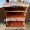 A tallboy hand-painted cabinet that features an upper section with an open shelf and a lower section with drawers, all painted red inside. The exterior showcases a textured pink design with black marks. It is surrounded by decorative items including a tray, vase, and small plants. Suitable as linen cupboard or linen press, this upcycled piece can be used as bedroom storage, kitchen storage, or clothes storage.