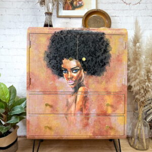 A hand-painted Tallboy cabinet features a vibrant painting of a woman with curly hair against a warm-toned background. The cabinet rests on black hairpin legs and is surrounded by various plants, a decorative plate, and a framed picture of a cow on a white brick wall.