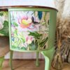 Introducing the exquisitely restored Queen Anne Painted Walnut Bedroom Set, featuring a vintage dressing table/vanity and stool. This mint green piece boasts hand-painted floral accents, with two drawers on the left side adorned with vibrant tropical flowers and leaves. The elegant dressing table stands on gracefully curved legs, complemented by a white brick wall backdrop and pampas grass decor nearby.