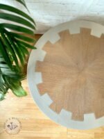 An MCM Circular Round 'Cog' Coffee Table by Nathan Furniture, featuring a hand-painted soft khaki beige finish and a distinctive jagged-edge border, is placed on a light wood floor next to a green potted plant. The "BUILD IT & RESTORE IT" logo is visible in the bottom left corner.