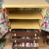 Introducing our Hand-painted Tropical Tallboy! This unique upcycled cabinet features a vibrant yellow top section with two open shelves. Below, you'll find three brown drawers with floral and elephant-patterned interiors. The sides and drawers are adorned with tropical-themed wallpaper, adding an exotic touch to any room. Perfect for bedroom storage, kitchen storage, or clothes storage, this tallboy sits beautifully on a wooden floor surrounded by plants.