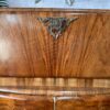 Close-up of the Rivington Cocktail Cabinet, featuring vintage Art Deco design with intricate detailing at the top center. The rich walnut and polished green and gold finish are visible, with decorative monstera leaves adding an elegant touch. The background includes a decorative, radial mirror reflecting its retro charm.