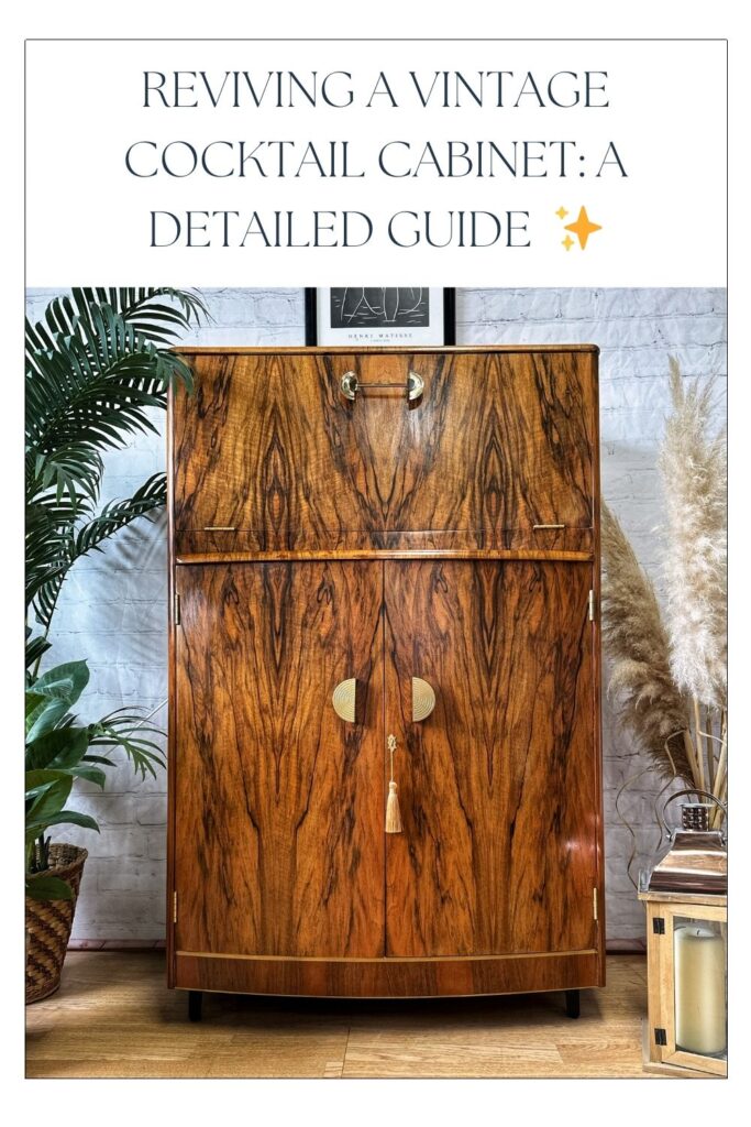 A stylish vintage cocktail cabinet made of wood with a detailed grain pattern. It features dual doors with gold handles and a tassel. The background includes a green plant, dried pampas grass, and a framed artwork. Text above reads "Reviving a Vintage Cocktail Cabinet: A Detailed Guide.