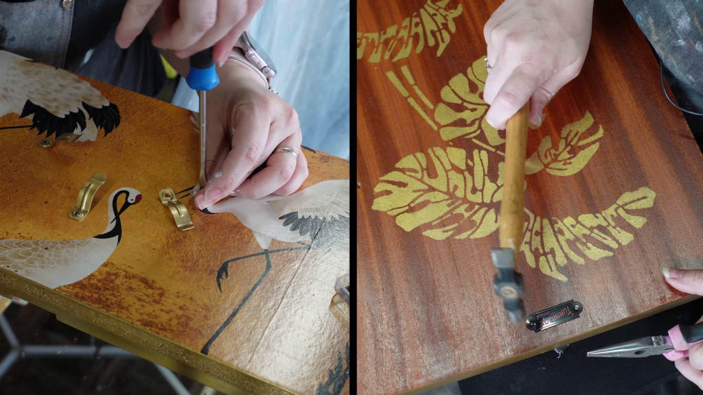 Split image showing two hands working on wooden surfaces. Left: Hand using a screwdriver to fix a small brass hinge on a decorated board with images of cranes. Right: Hand using a hammer to tap a small tool on a wooden board with gold leaf-style leaf patterns.