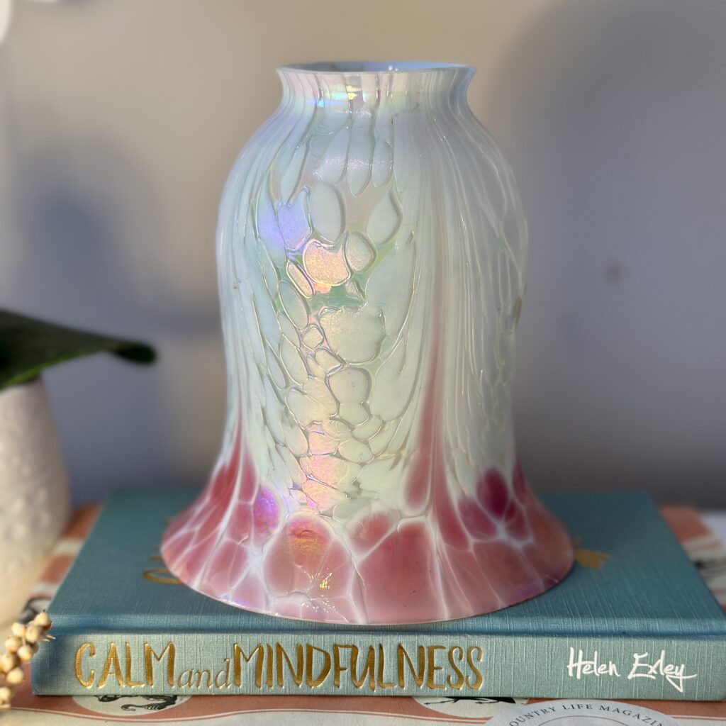 A decorative vase with iridescent pink, purple, and white patterns sits atop a book titled "Calm and Mindfulness." The vase reflects light, creating a serene ambiance. The artist's signature, Helen Eley, is visible in the corner.